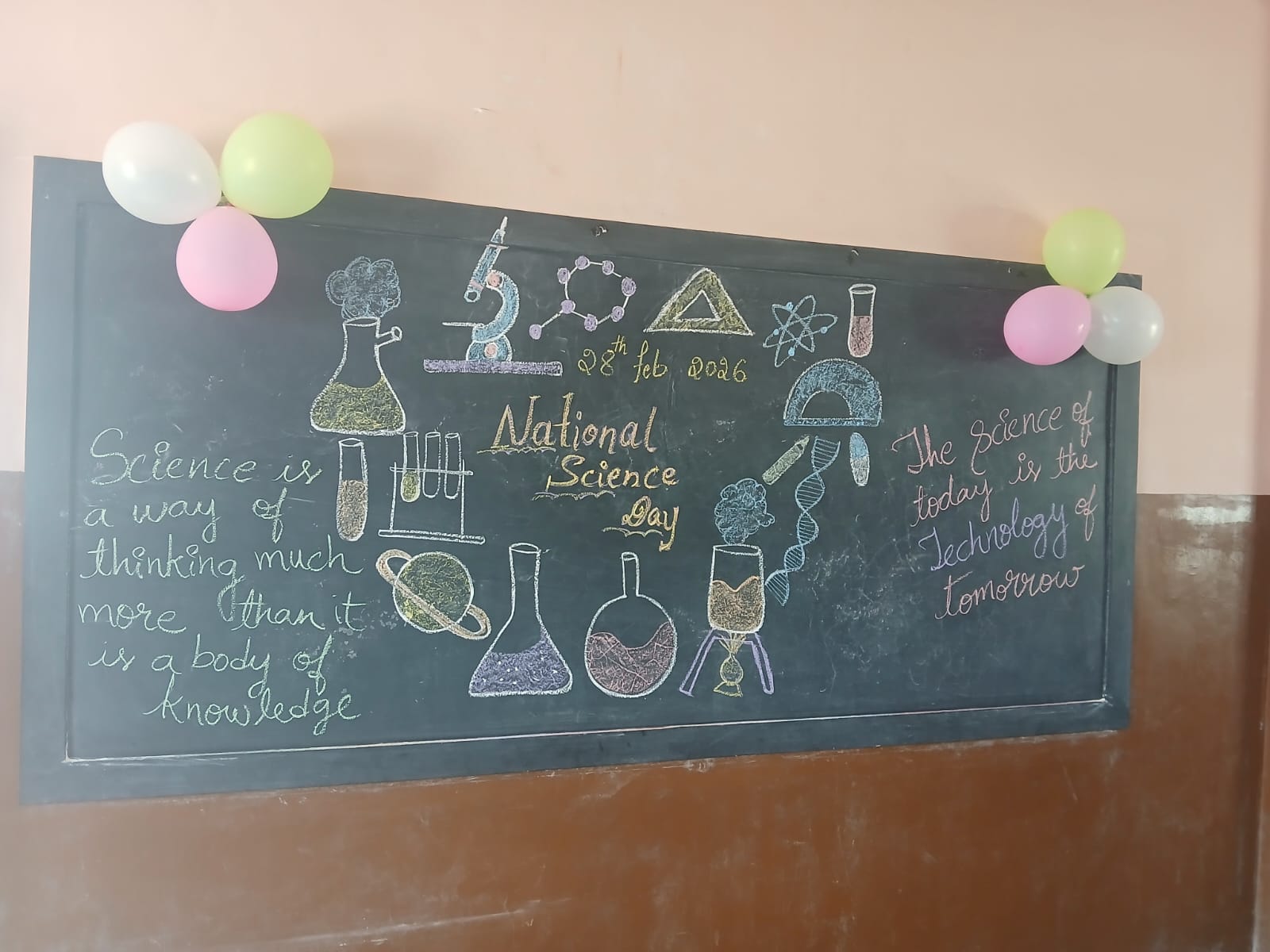 A colorful blackboard decorated with science drawings and balloons celebrates National Science Day.