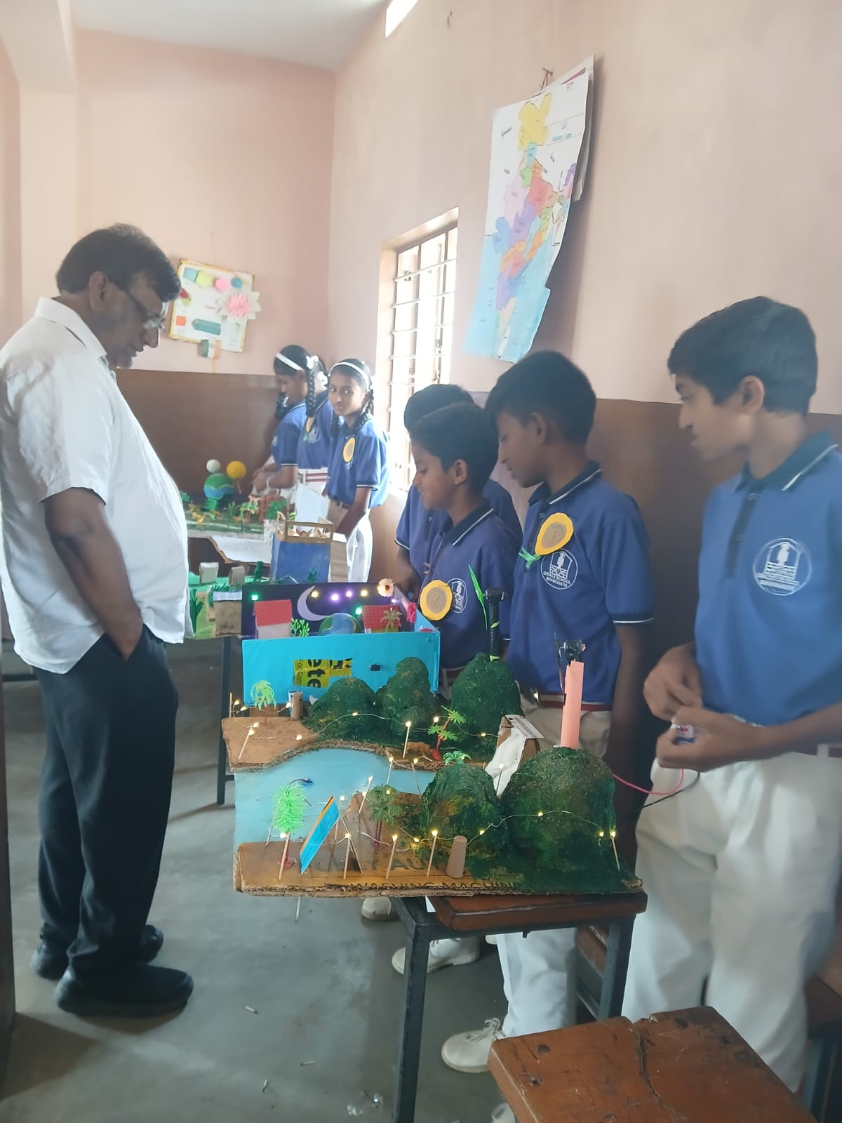 A group of boys showcase an illuminated landscape model demonstrating scientific concepts.